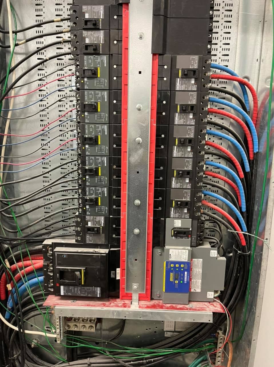 Panel de distribución abierto con interruptores termomagnéticos y conductores ramales identificados por color.